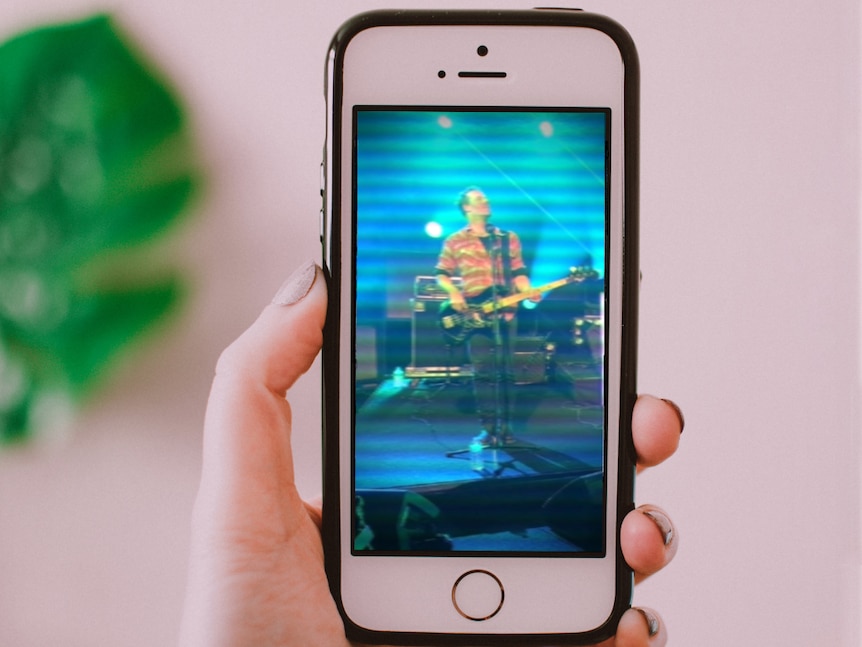 A hand holds a phone showing a musician playing bass guitar