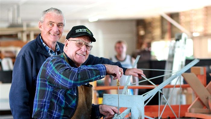 Two men standing together with one holding a tool.