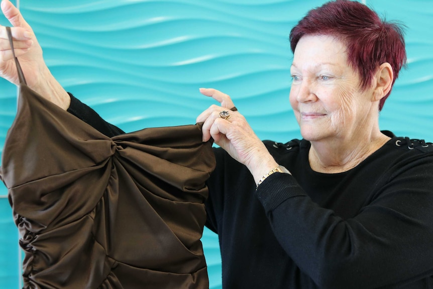 A woman holding up a formal dress and looking at it