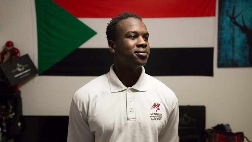 Akang Akang poses for a portrait in front of a Sudanese flag in his bedroom.