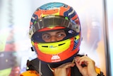 An F1 driver does the buckle on his multi-colour helmet, with his visor up