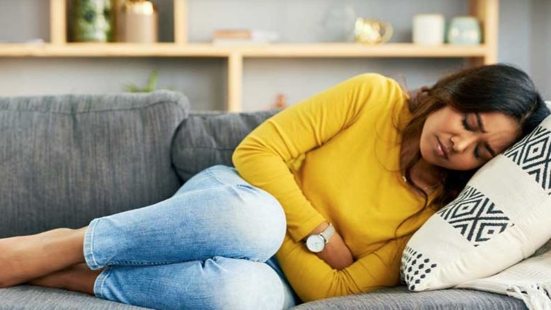 A woman in a yellow top and teens clutches her stomach on a couch 