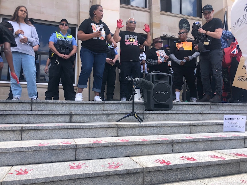 Protesters outside WA Parliament House with red hand prints on the steps in front of them.