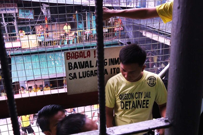 A crowded court yard in Quezon City Jail, seen through the wire cage of a stairwell.