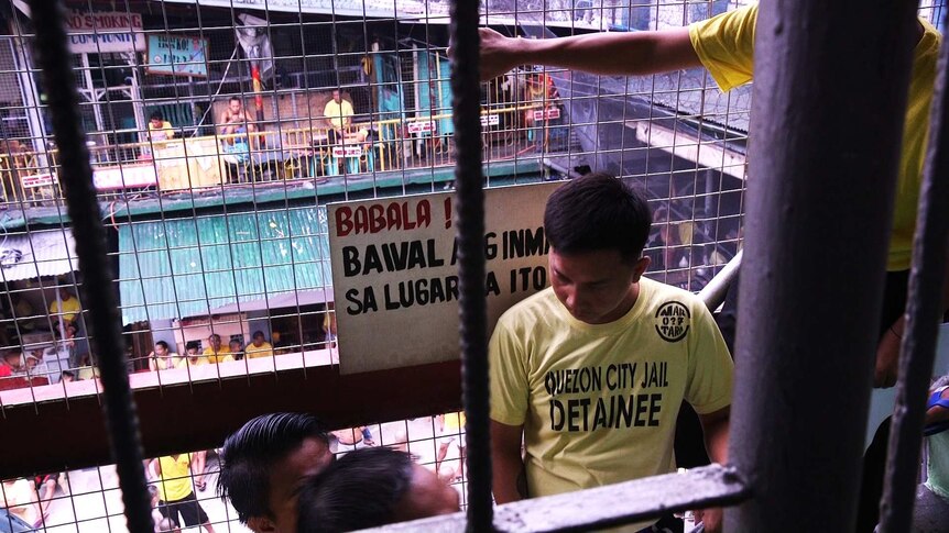 A crowded court yard in Quezon City Jail, seen through the wire cage of a stairwell.