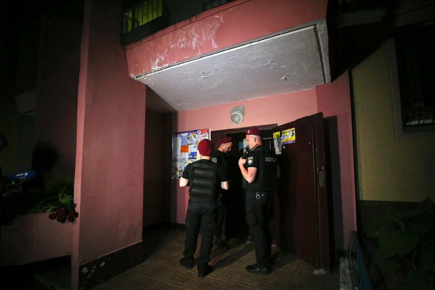 Three police officers stand at the front door of a building.