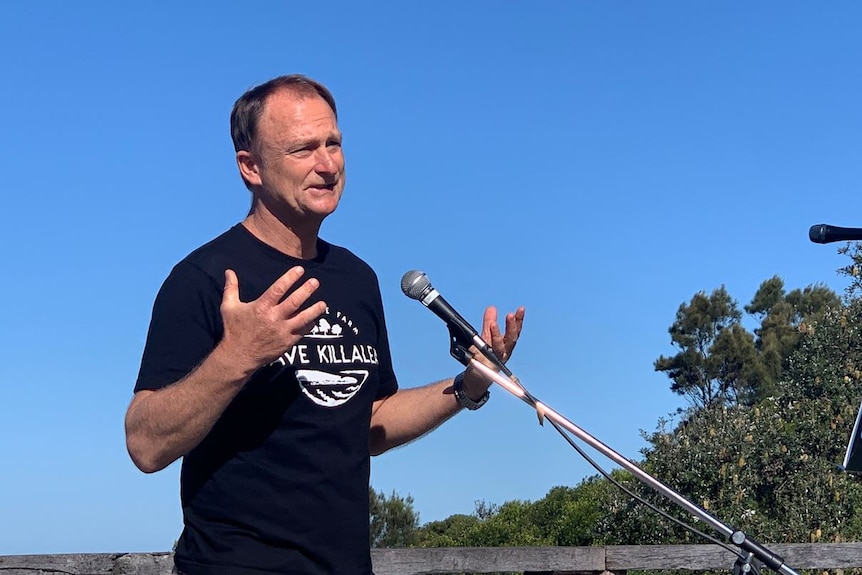 Man stands talking in front of a microphone