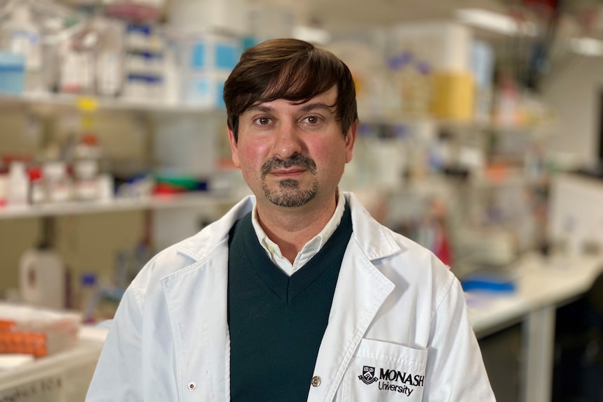 Dr Keith Al-Hasani, wearing a white lab coat, smiles calmly at the camera.