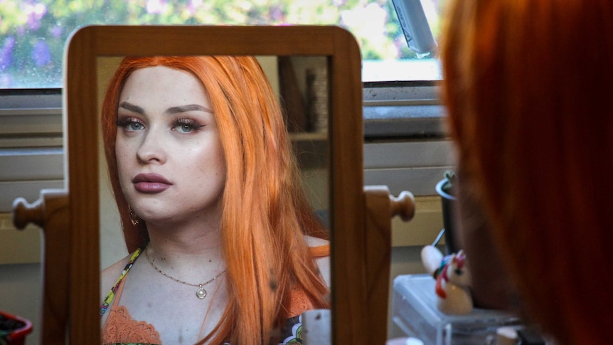 Transgender teenager Aliza looks at her finished make-up in the reflection of a mirror