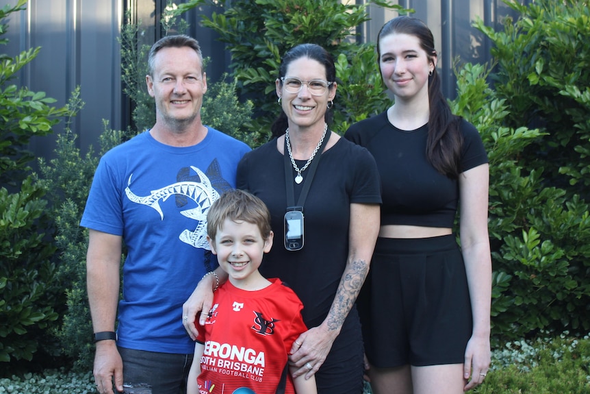 An image of the Heath family standing outside in front of bushes and hedges in front of a brown wooden fence