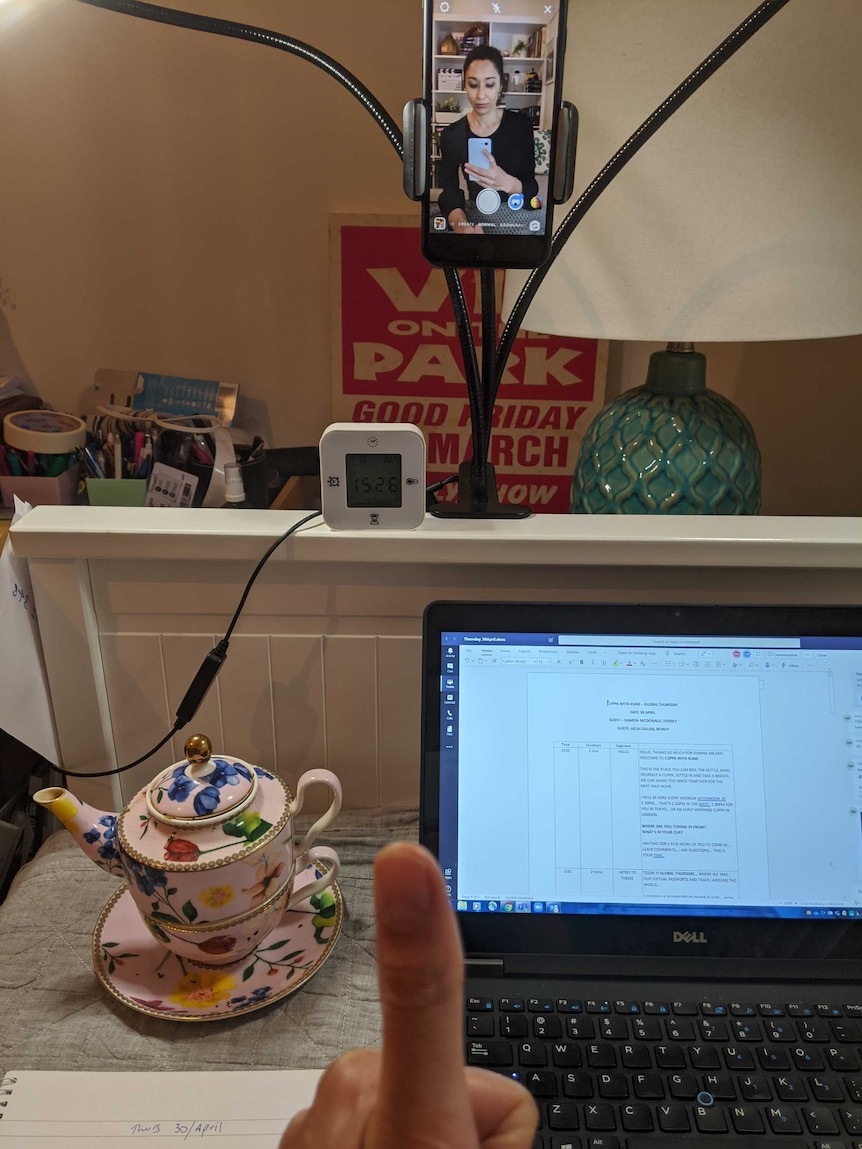 Mobile phone on stand with Kumi on screen on top of computer at desk with teapot alongside.