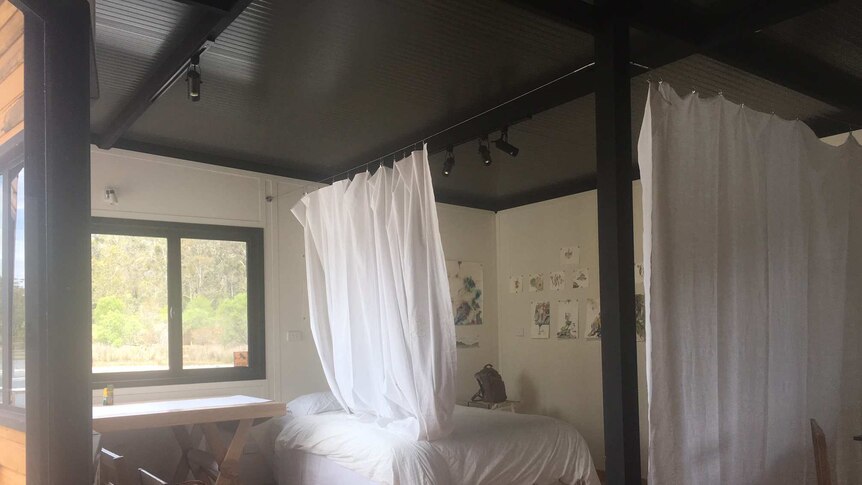 A bedroom with a bed with white sheets and white sheets hanging from the ceiling over the bed
