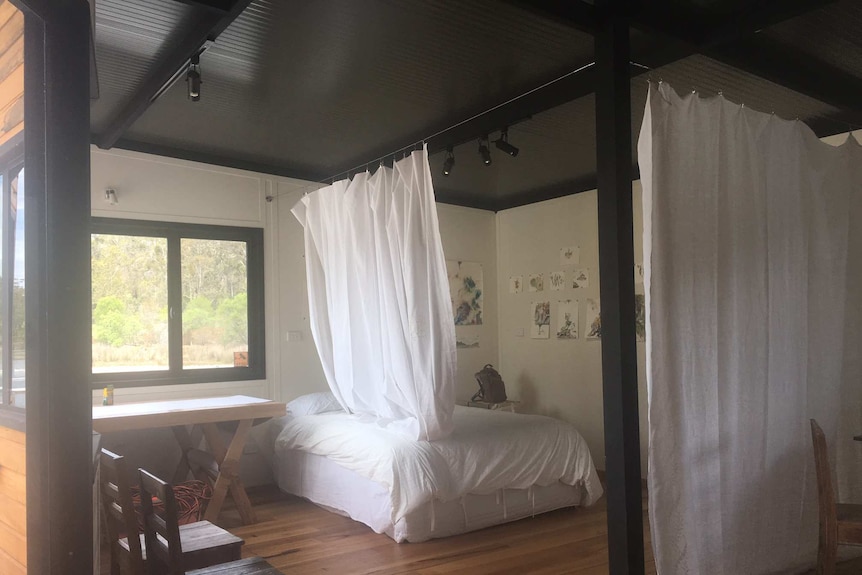 A bedroom with a bed with white sheets and white sheets hanging from the ceiling over the bed