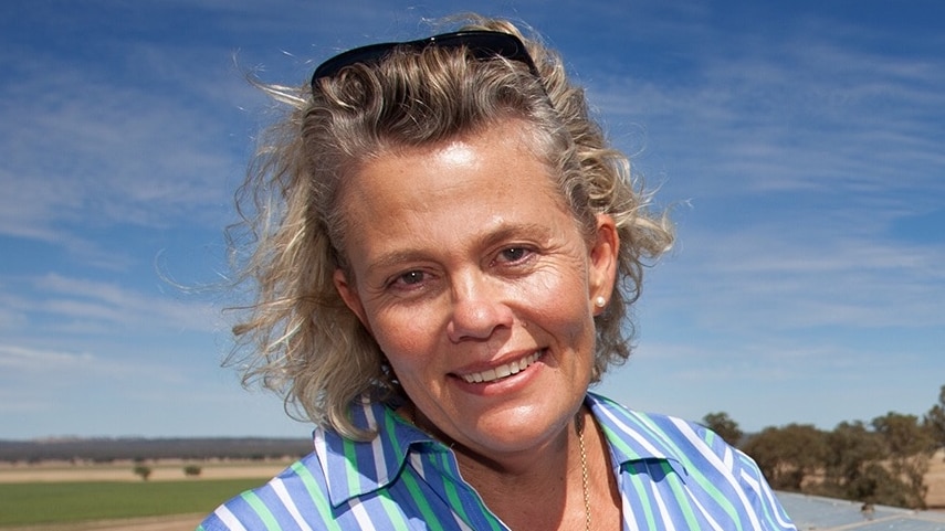 A woman with sunglasses in her hair against a wide blue sky and wide open green plains, Liverpool Plains, New south wales