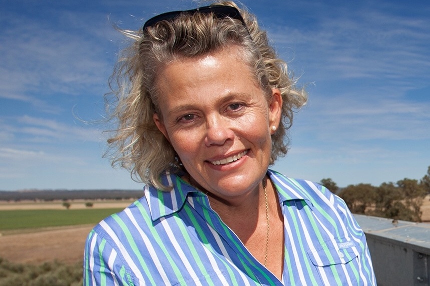 A woman with sunglasses in her hair against a wide blue sky and wide open green plains, Liverpool Plains, New south wales