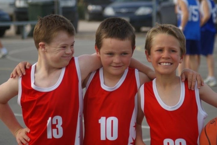 three boys stand together wearing basketball singlets 