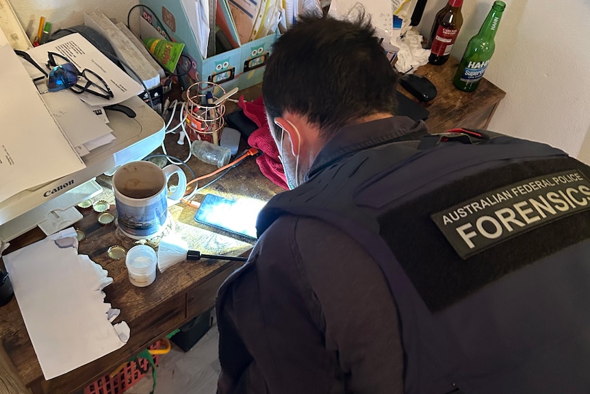 AFP officer stands over a desk fingerprinting items