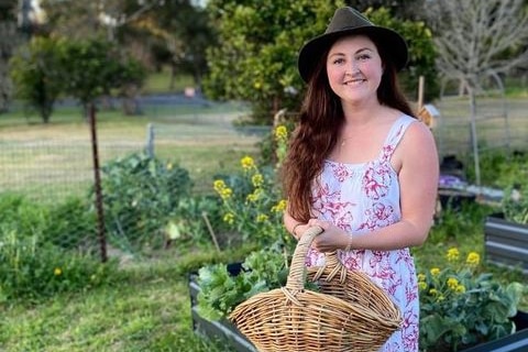 A woman wearing a hat and holding a basket in a garden.