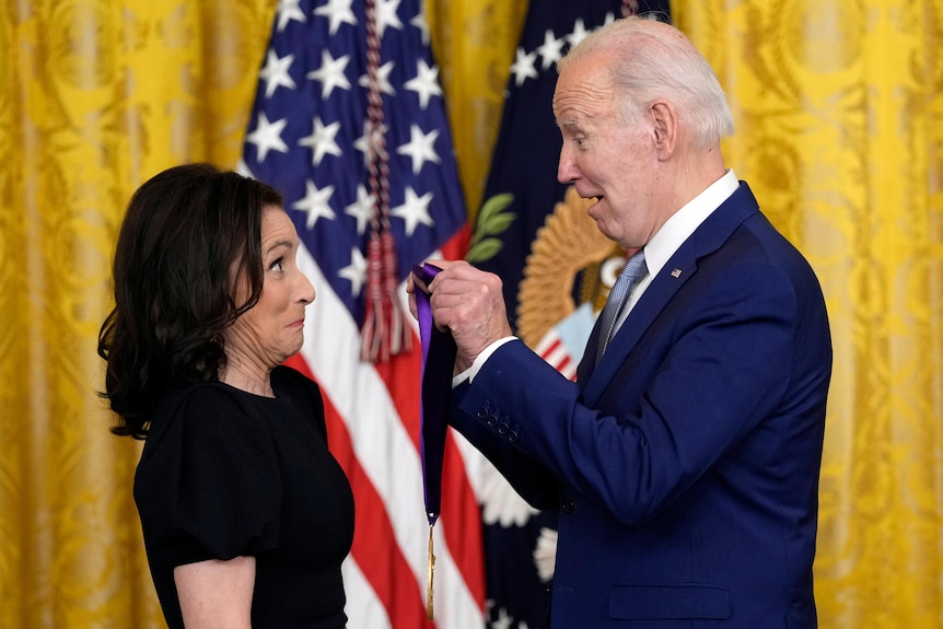 Julia Lous-Dreyfus pulls a funny face as Joe Biden holds a medal on a purple ribbon