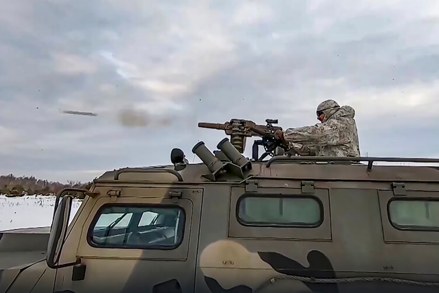 A russian soldier in uniform fires a weapon on the roof of a vehicle in Belarus