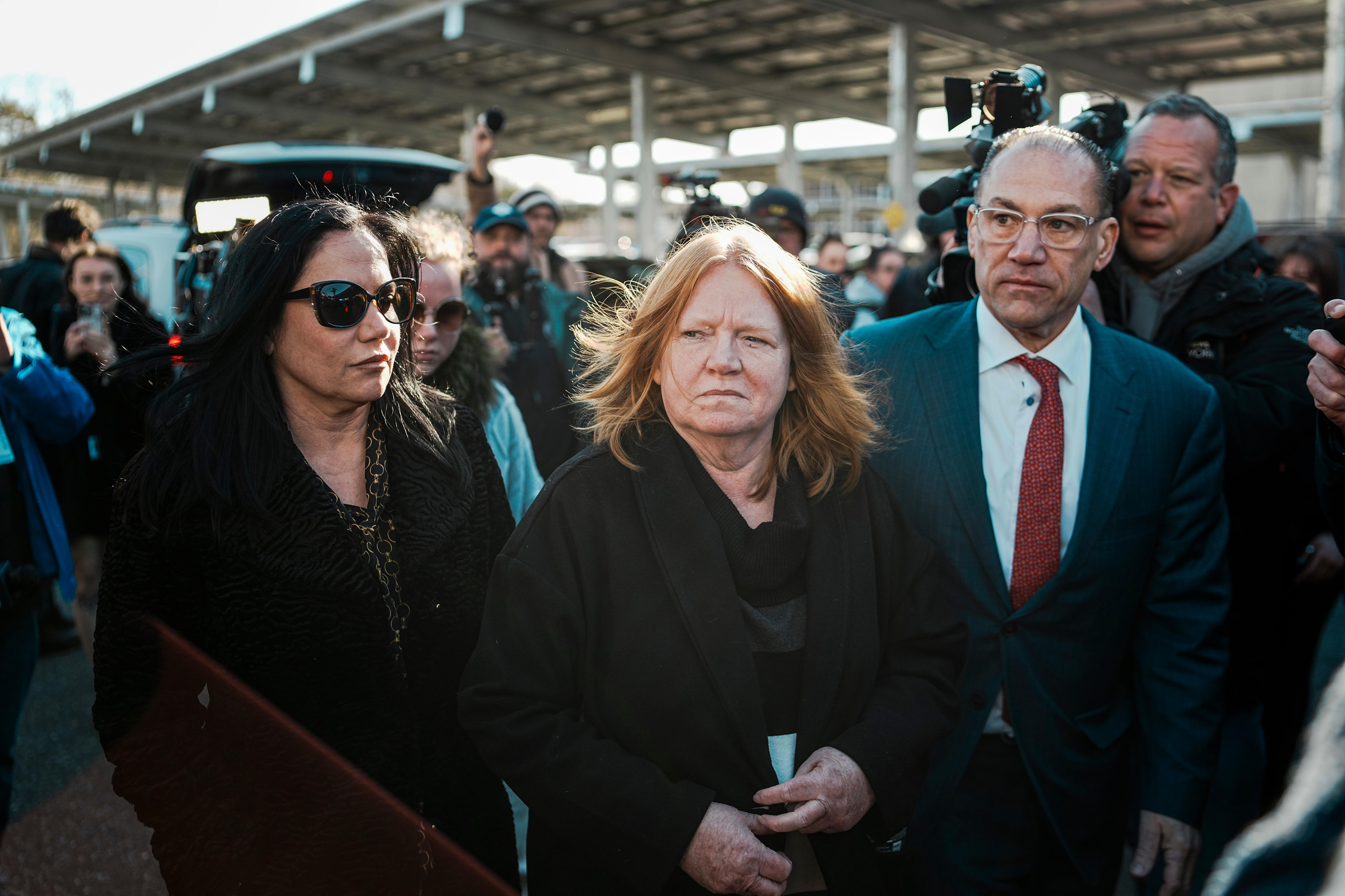Two women and a man in a suit arriving out the front of a busy courthouse.