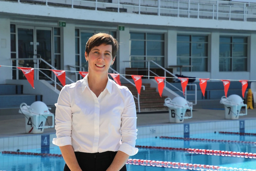 Mid shot of a woman in a white shirt standing in front of red bunting over a swimming pool.