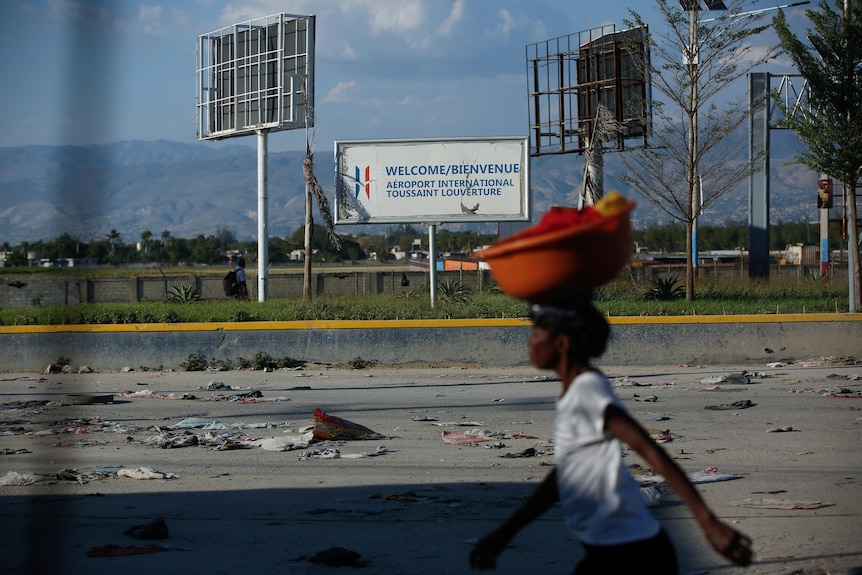 A girl with a bowl on her head walking past an airport with debris scattered in front. 