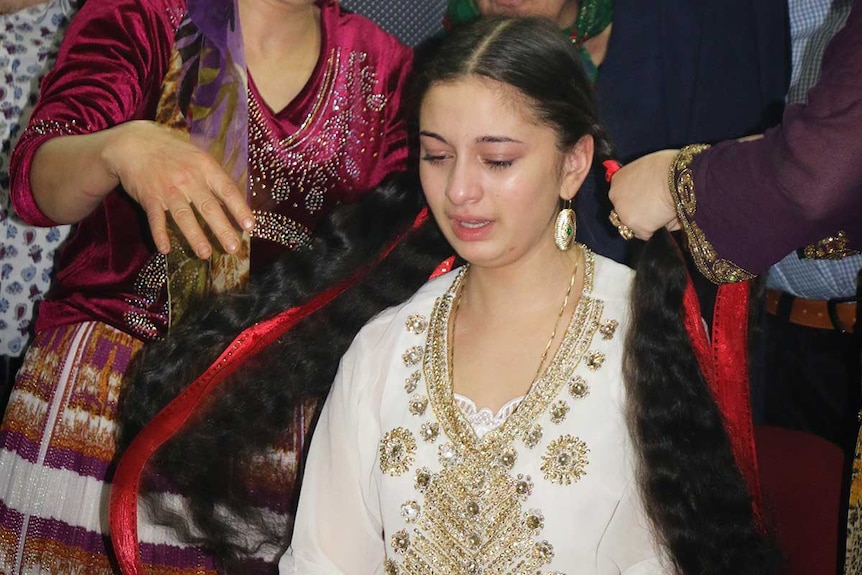 Young girl cries as an older woman  unravels her hair, sympbolising the end of maidenhood.