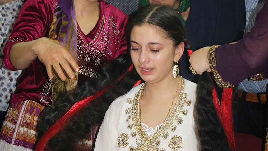 Young girl cries as an older woman  unravels her hair, sympbolising the end of maidenhood.