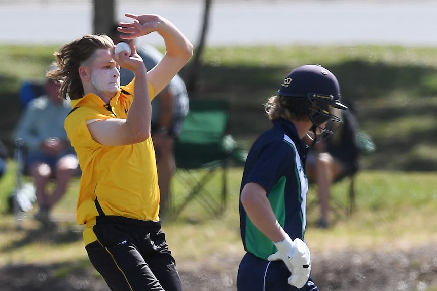 A cricketer with sunscreen on his face bowls next to a batter facing away.