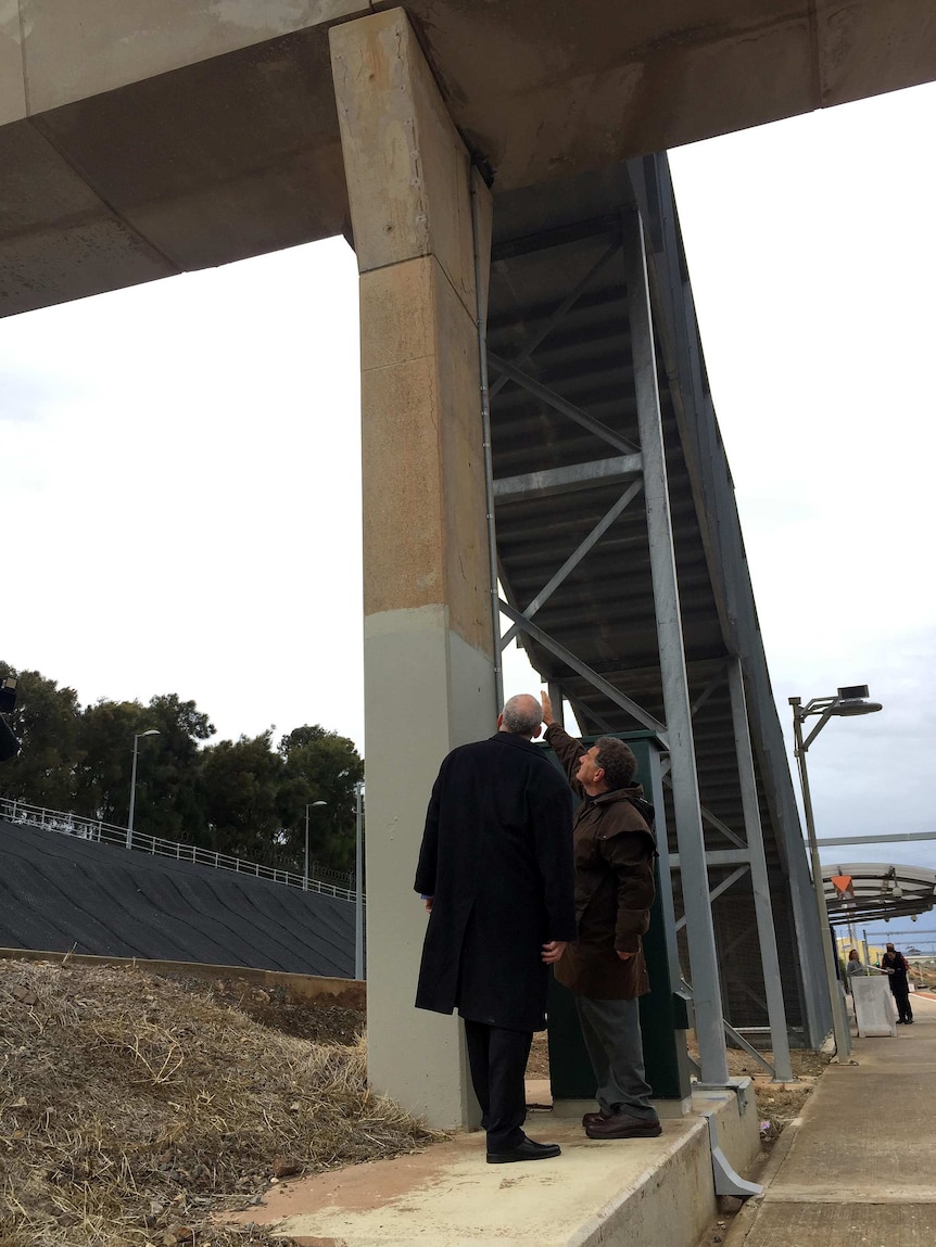 Two men look at cracked concrete in a pillar of the Lonsdale overpass.