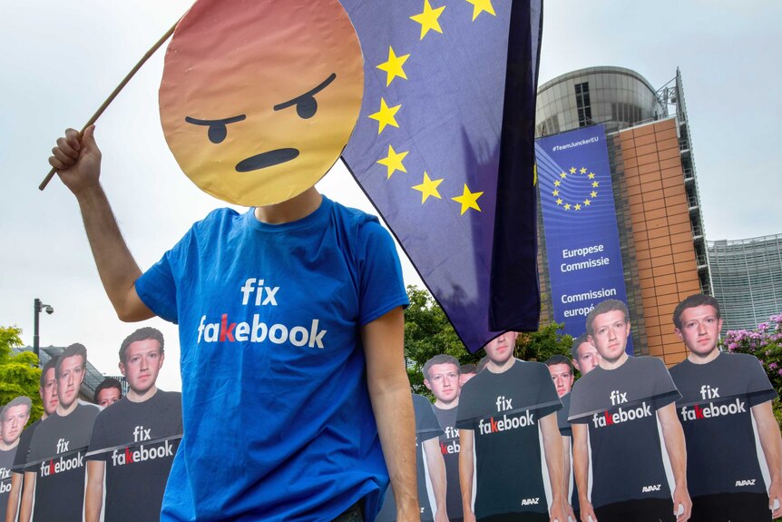 A protesters wearing a 'fix fakebook' t-shirt leads others carrying Zuckerberg cardboard people.