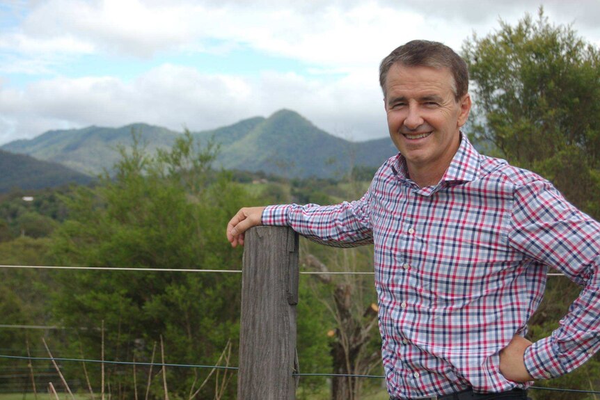 LNP Senate candidate for Queensland Gerard Rennick stands with his arm on a fence with mountains and countryside behind him.