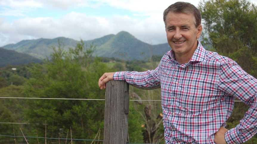 LNP Senate candidate for Queensland Gerard Rennick stands with his arm on a fence with mountains and countryside behind him.