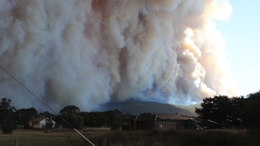 Large thick billows of white smoke rise from the hills, with a house in the foreground.