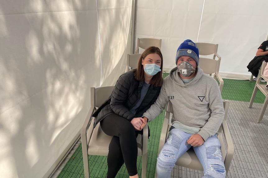 A couple sitting on plastic chairs after getting COVID jab