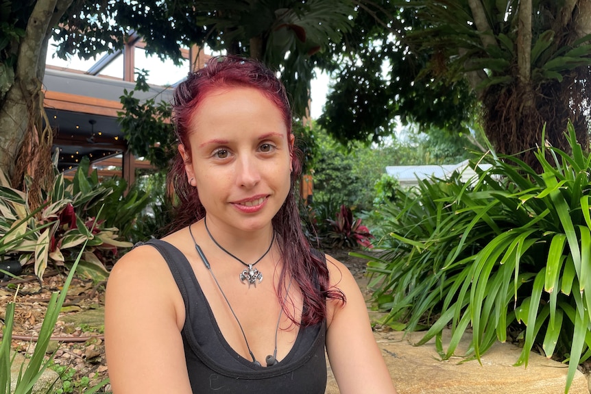 A smiling red-haired woman sitting under a large tree