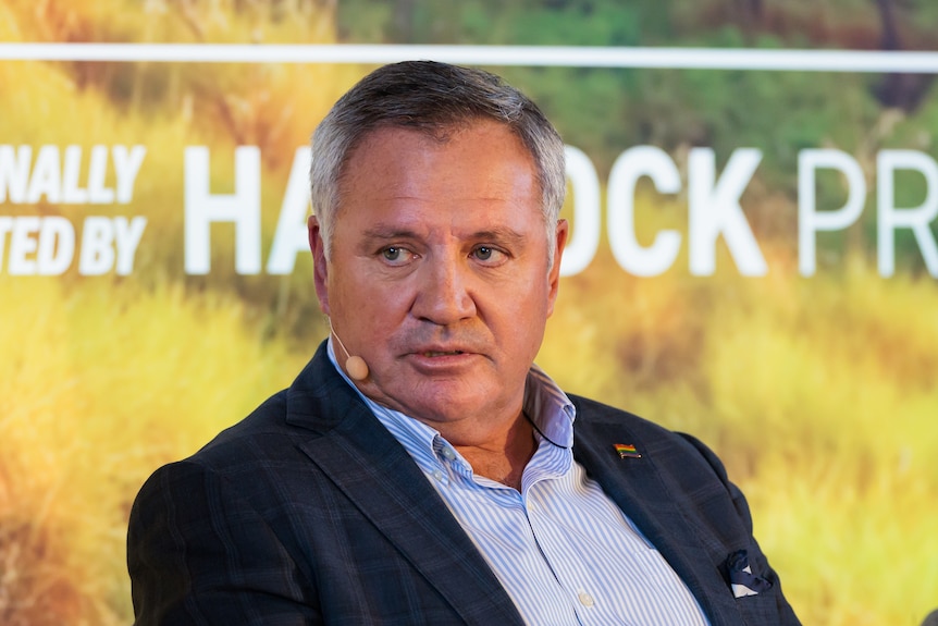 A man in a suit with a headpiece microphone speaks at what looks like a panel event. Mid-shot.