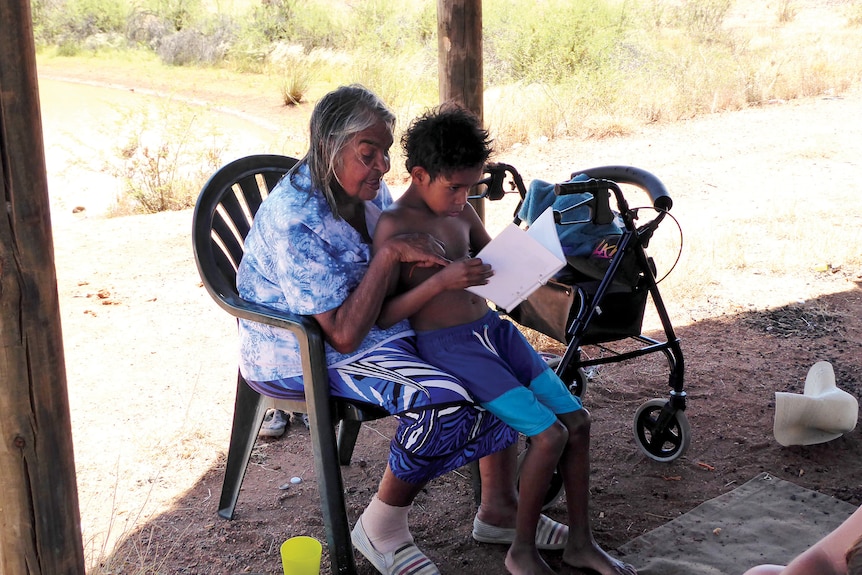 A woman reads to a child sitting on her lap