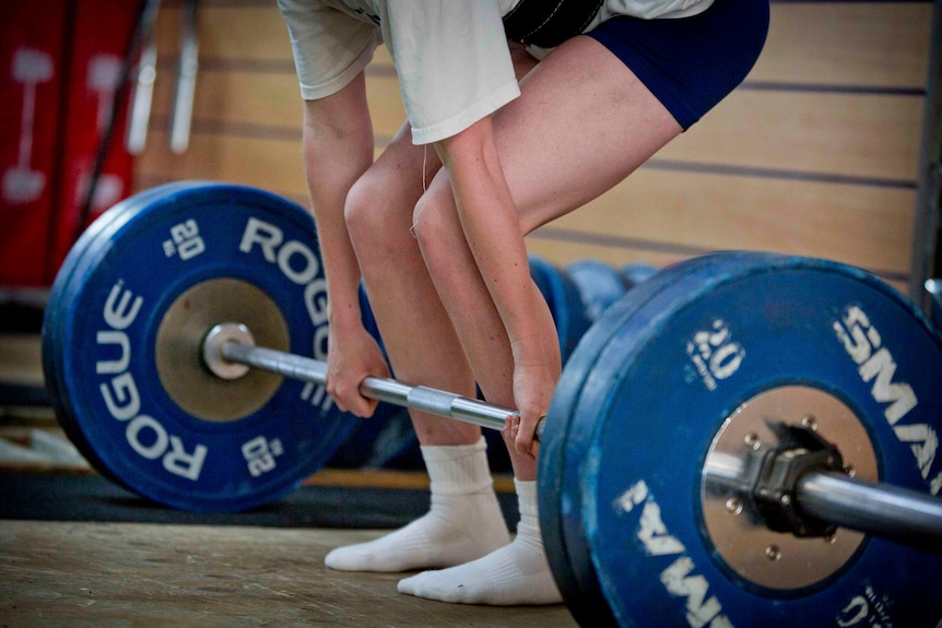 A young woman stands with her hands gripping a barbell weighted with 80kg as she prepares to perform a deadlift