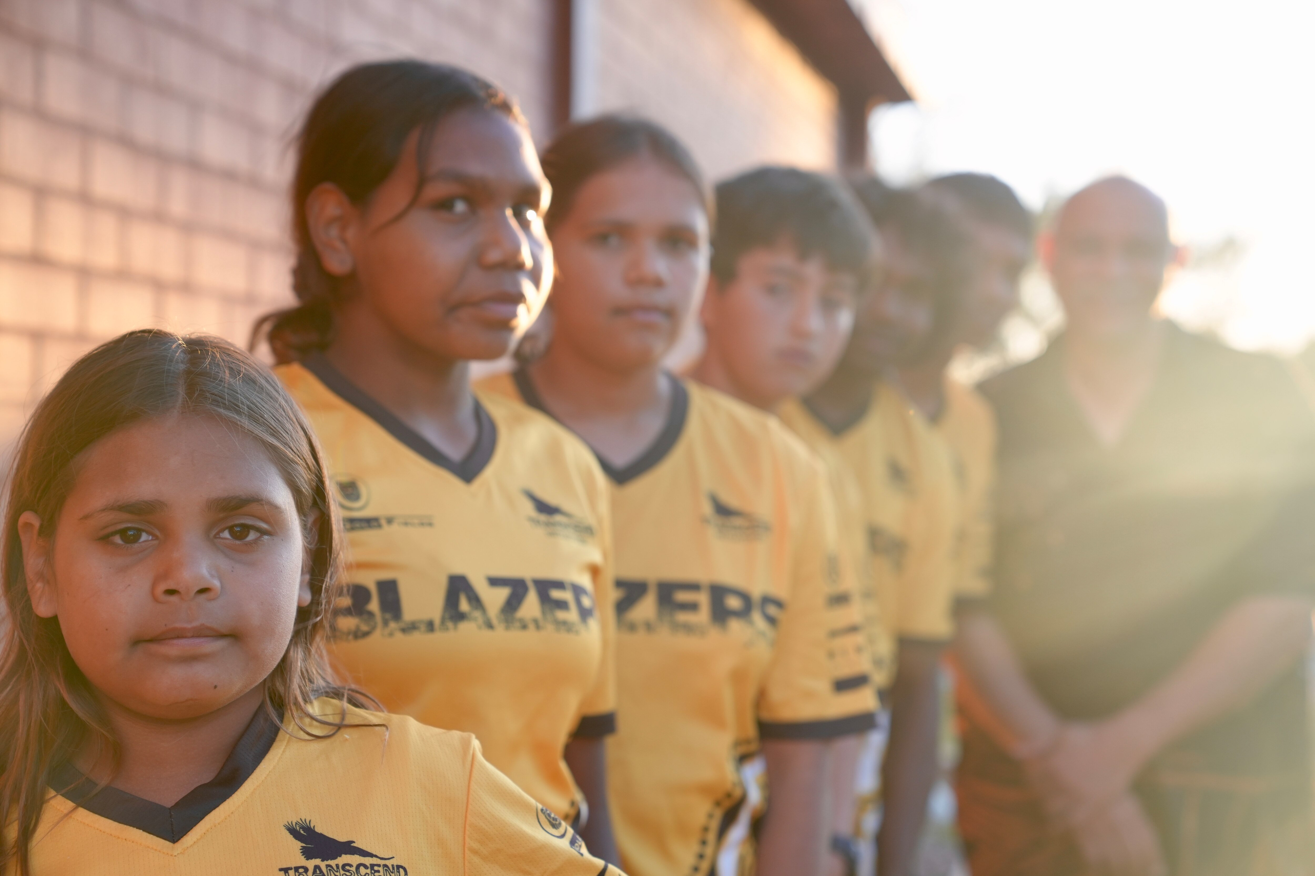 Children stand in a line wearing yellow basketball shirts with the word "Blazers".