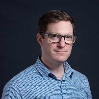 Man wearing glasses and blue checkered shirt with a black background