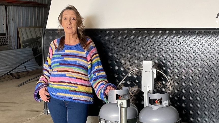 A woman stands next to gas bottles on a caravan