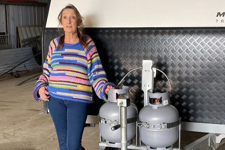 A woman stands next to gas bottles on a caravan