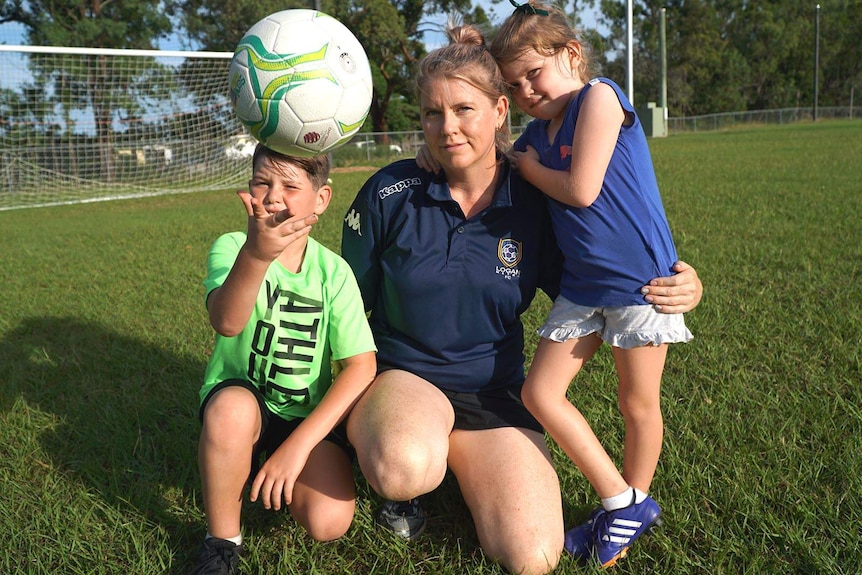 A mother with her two children crouched on a soccer pitch