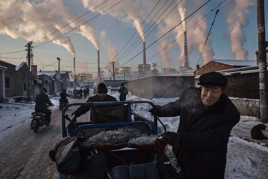 Chinese men pull a tricycle in a neighbourhood next to a coal-fired power plant in China.