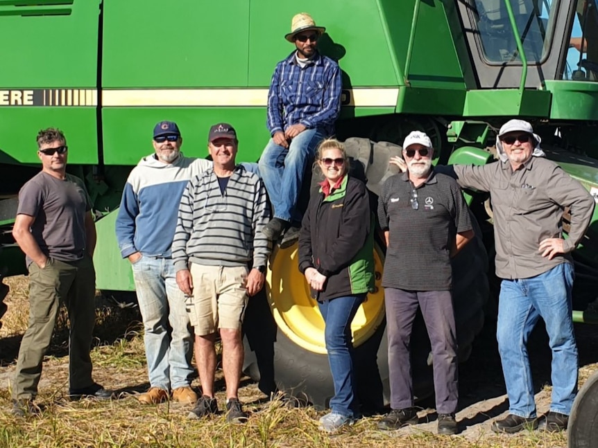 happy men stand in front of big green combine harvester