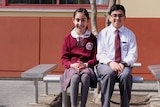 Assyrian school students Mary Anoya and Ramel Zia sit on a bench in uniforms.