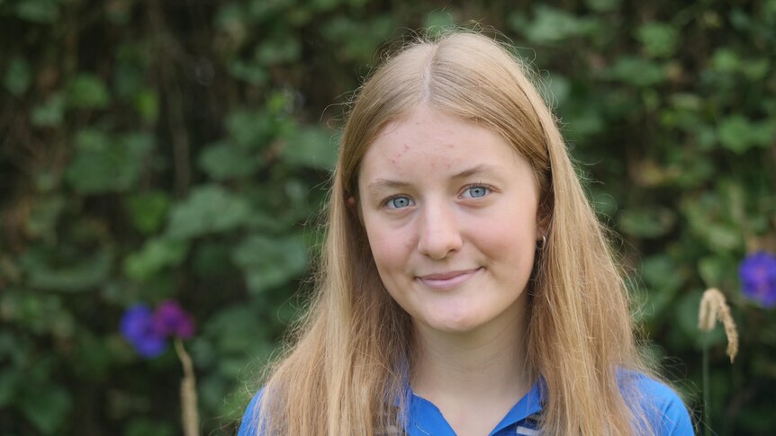 young blonde girl smiles at camera wearing a black polo t- shirt with a blue collar.  