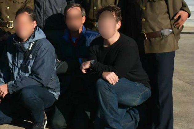 Three men with their faces pixellated from view kneel down for a group photo.